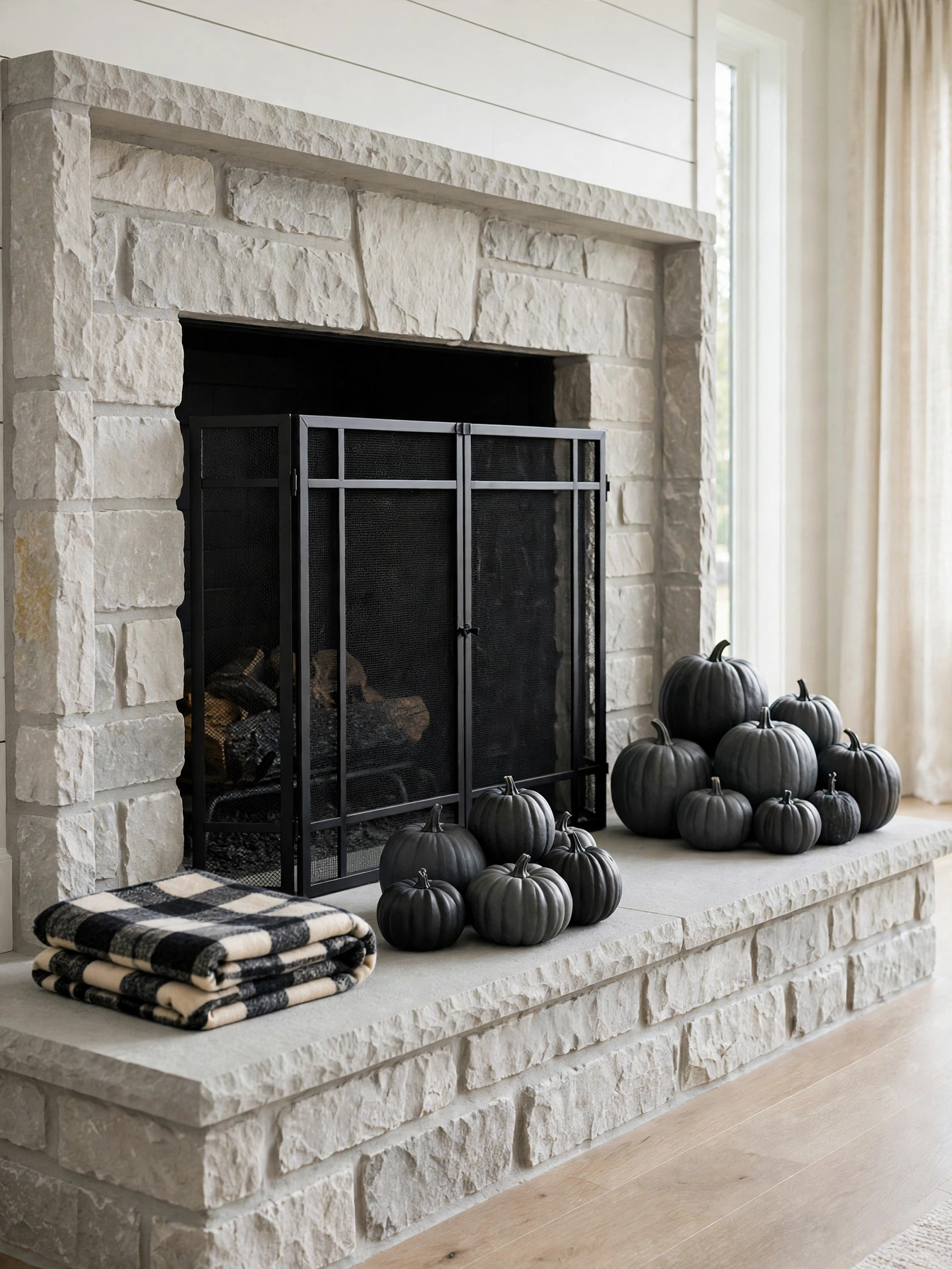 A fireplace hearth styled with a cluster of matte charcoal black and dark gray pumpkins in various sizes arranged on a lig...
