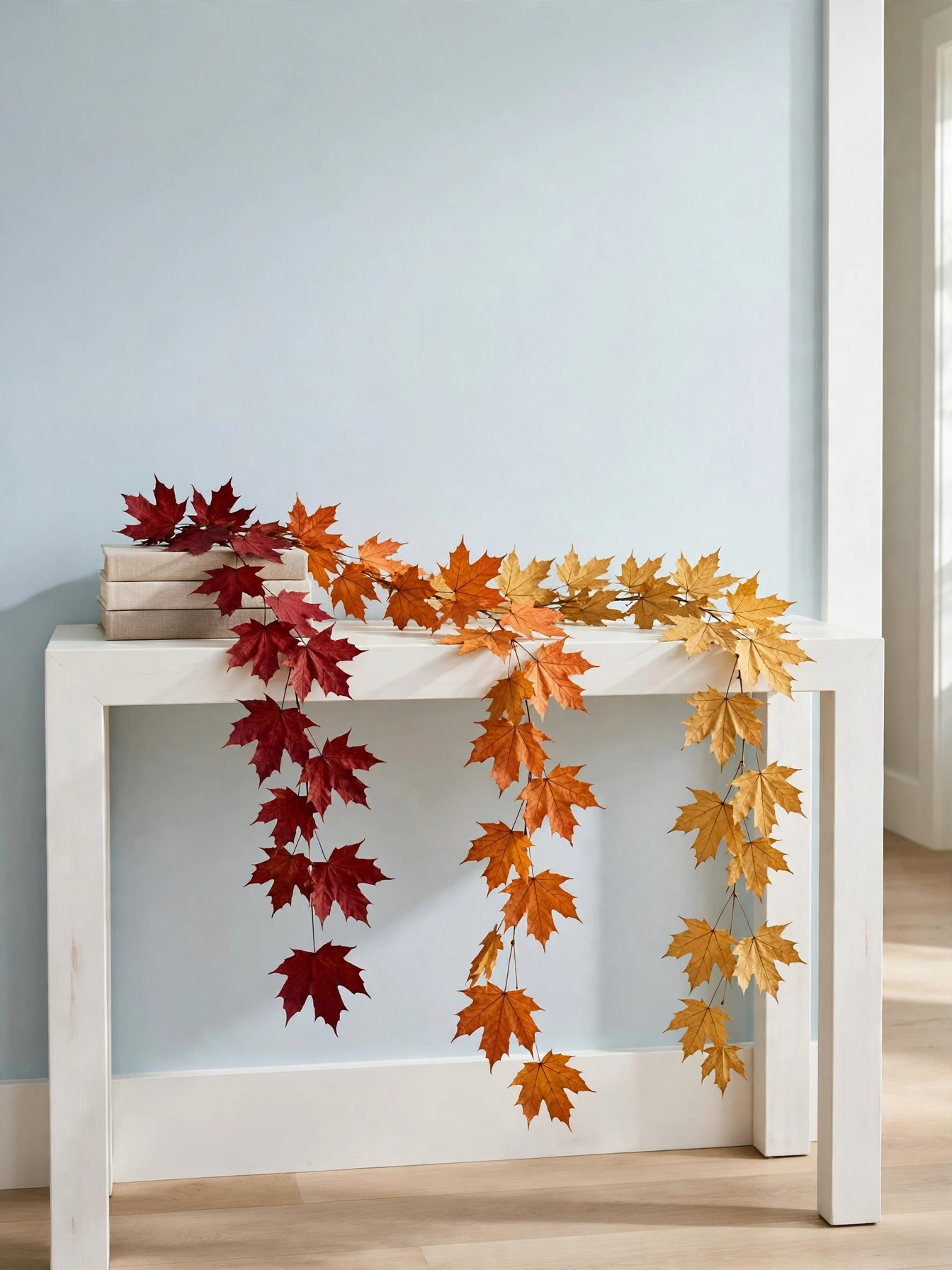 Fall entry table decor ideas for autumn 2026: preserved maple leaf strands in red and gold draped across a white console and trailing over the edge.