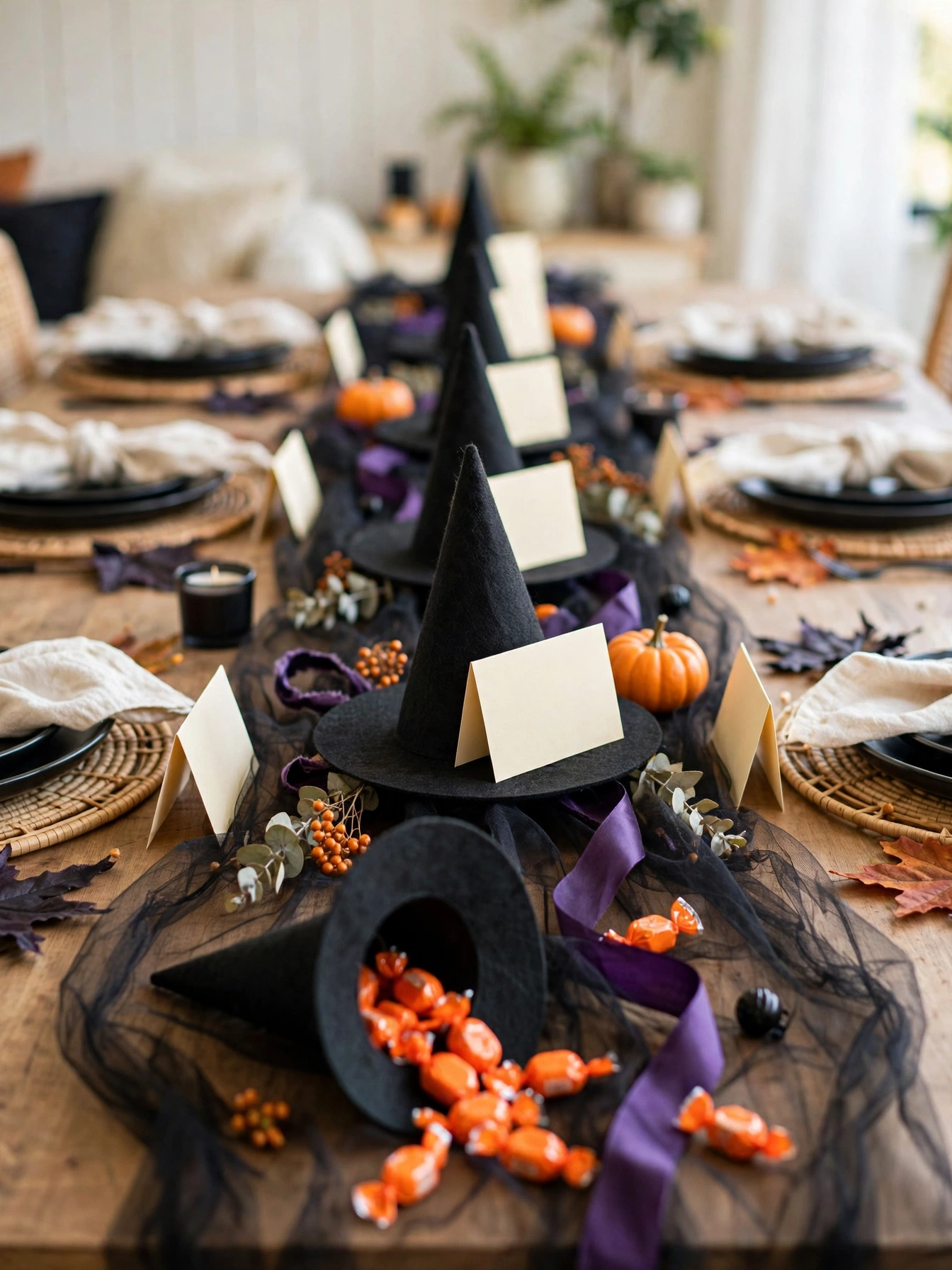 Mini black witch hats used as place card holders and favor cones in a row down the center of a dining table, with candy vi...