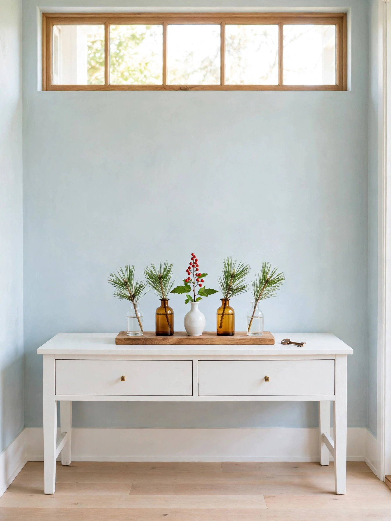 Christmas entryway table decor ideas 2026: five small bud vases in glass, amber, and ceramic holding pine sprigs and a red berry stem on a white console