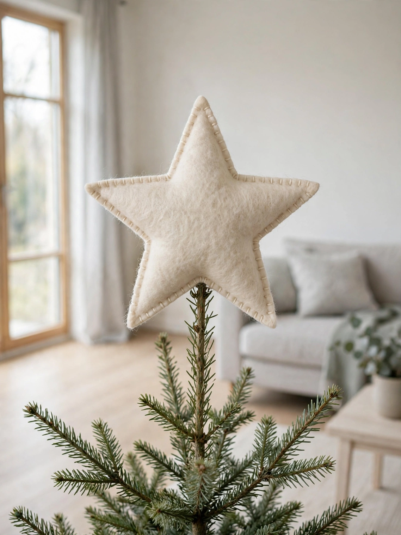 Cream wool felt star tree topper with stitched edges on a minimal tree in a bright room, one of the Christmas tree toppers ideas 2026