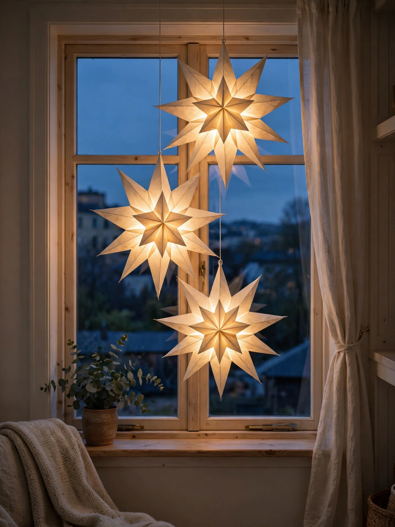 Glowing paper star lanterns hanging in a window at dusk with warm light shining through, one of the Christmas window decor ideas for 2026