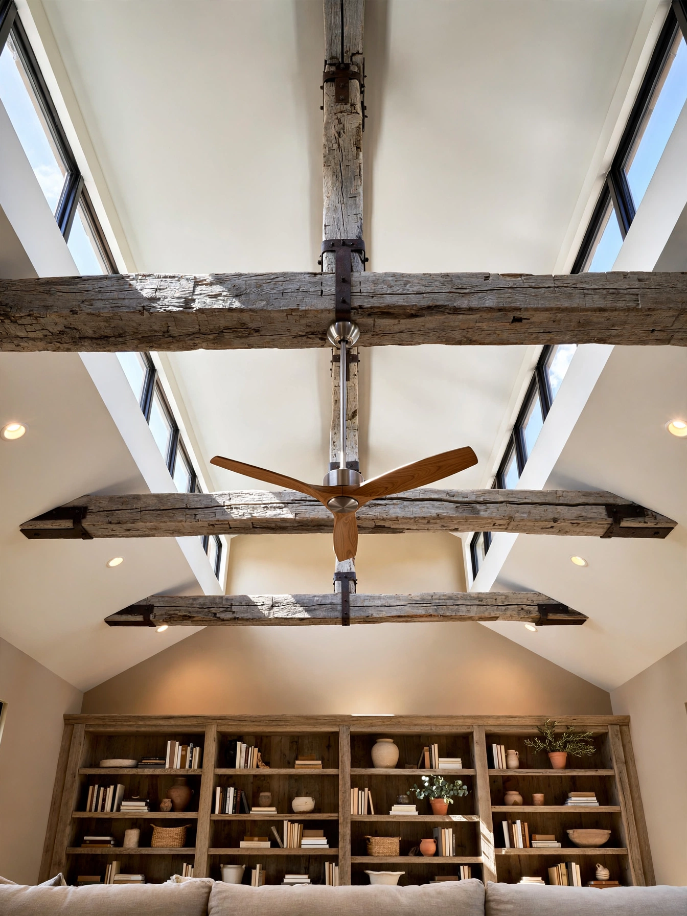 Exposed reclaimed barn beams on a vaulted ceiling in a modern western living room ideas great room with a steel ceiling fan